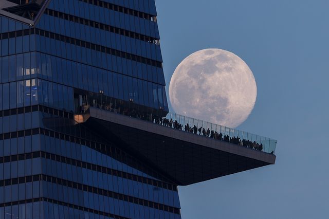 Almost full moon rises behind people standing on The Edge, the outdoor observation deck in Manhattan, March 16, 2022.